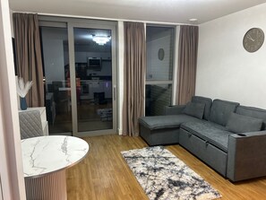 Ein modernes Wohnzimmer mit einem grauen Ecksofa, einem runden Marmortisch und einem gemusterten Teppich.