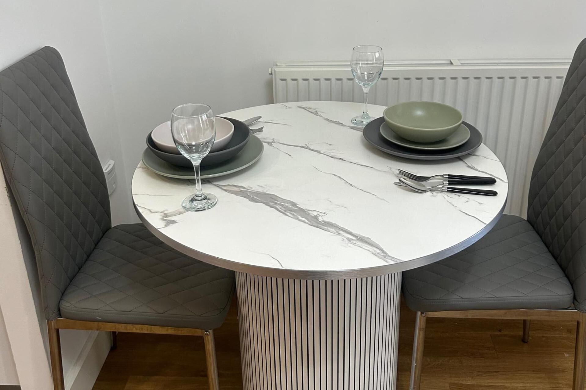 A round dining table with a marble top, surrounded by two upholstered chairs with a quilted pattern.