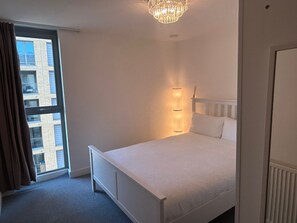 Ein Schlafzimmer mit großem Fenster, einem Bett, einem Nachttisch und einer Wandleuchte.
