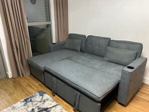 A grey sofa with a pull-out bed, a window with curtains, and a wooden floor. - Central 1-bed Apt for 4 Near Transport & Shops (London)