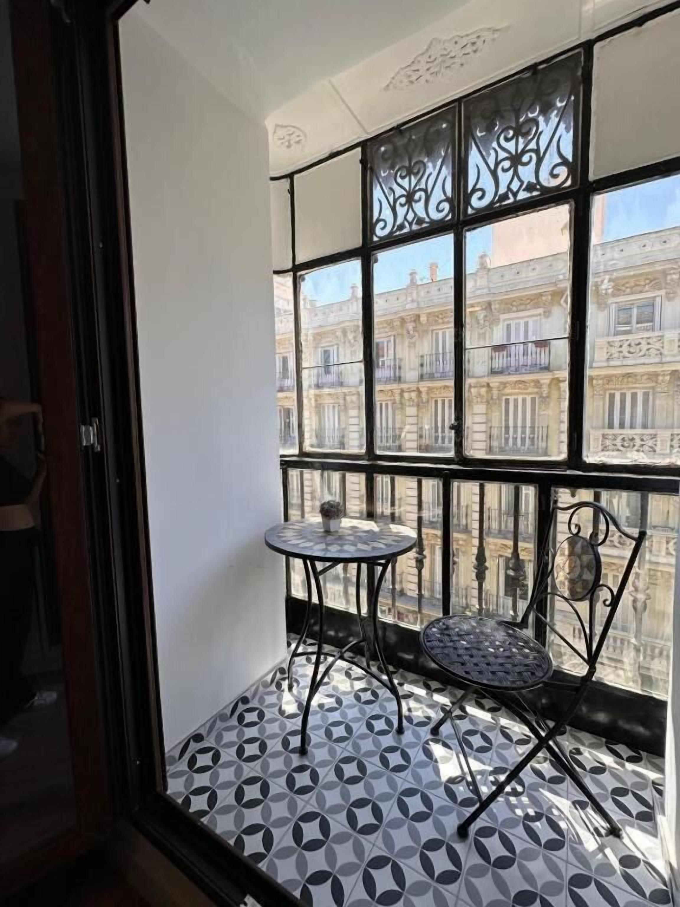 Ein kleiner Balkon mit einem gemusterten Boden, einem runden Tisch und einem Stuhl.