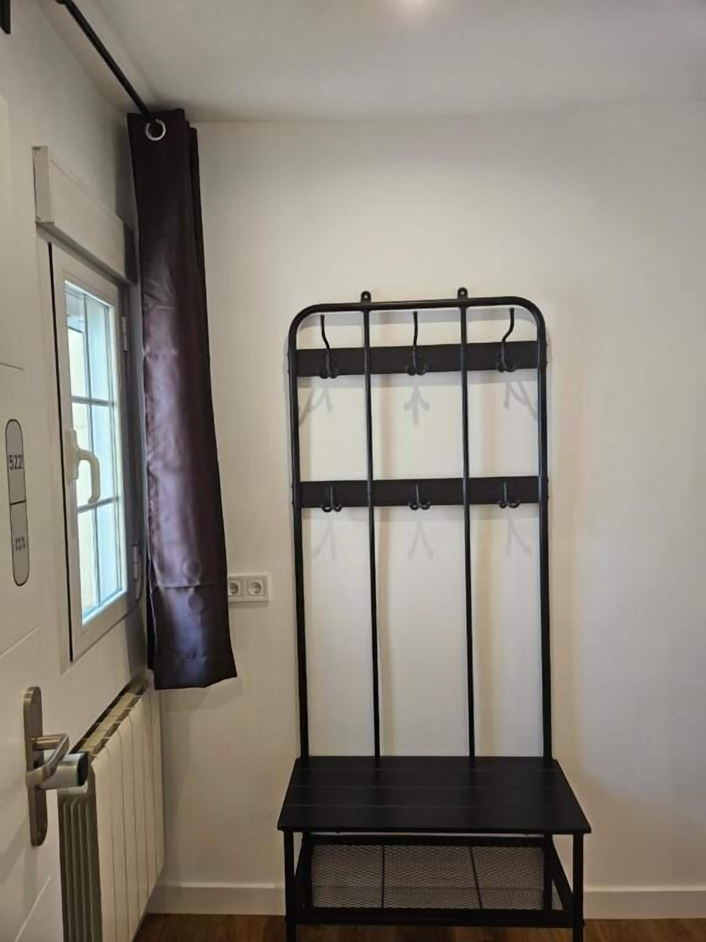 A room with a black metal rack with hooks, a window with a curtain, and a radiator.