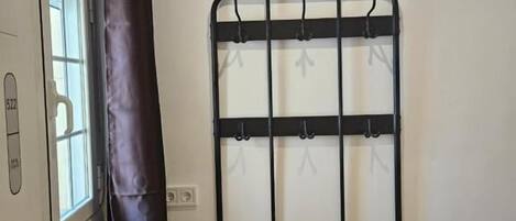 A room with a black metal rack with hooks, a window with a curtain, and a radiator.