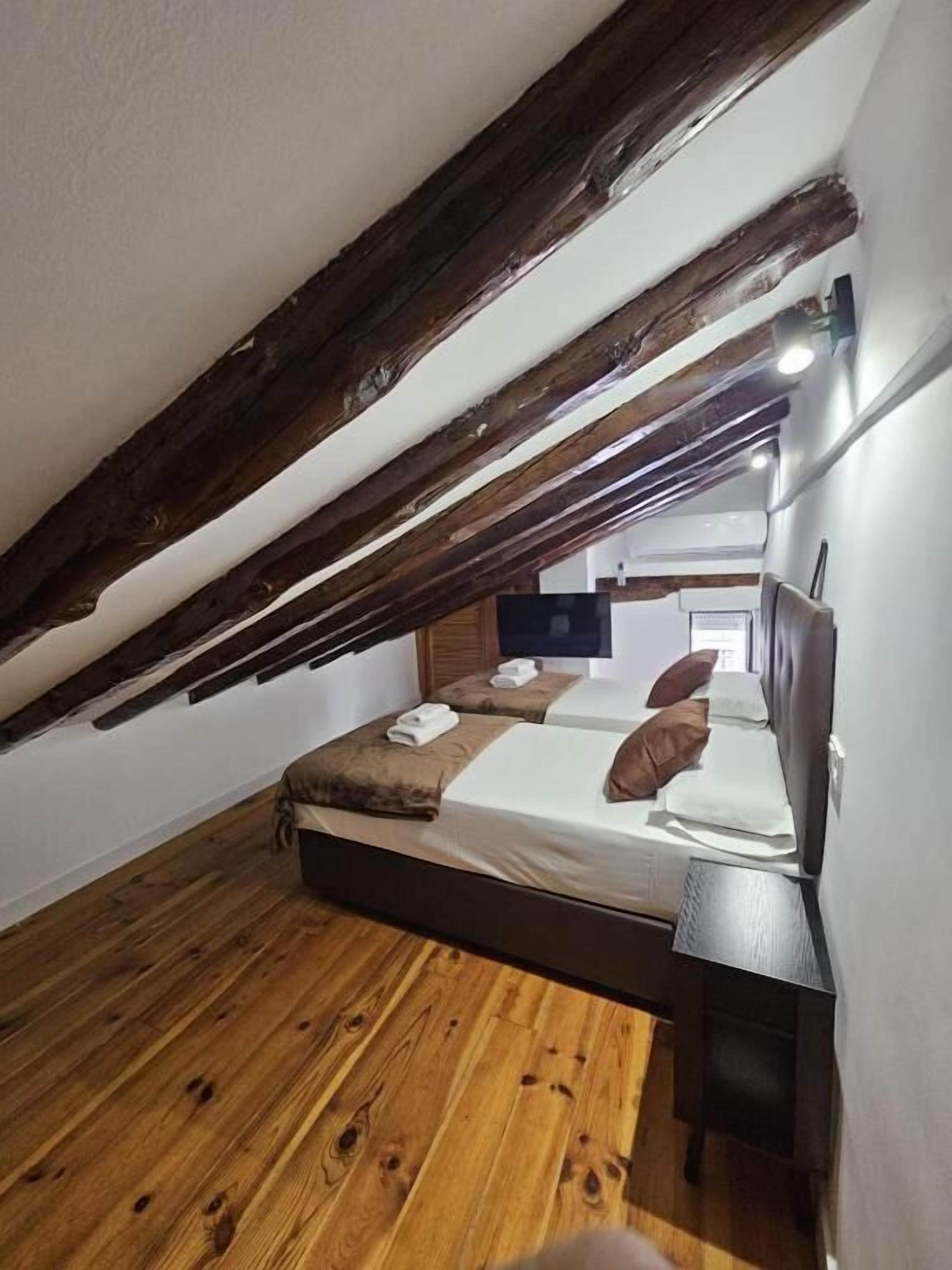 A small, cozy room with a sloped ceiling, wooden flooring, and a bed with pillows and a blanket.