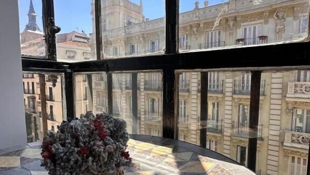 Una habitación de esquina con un ventanal grande, piso de baldosas y un arreglo floral sobre una mesa.