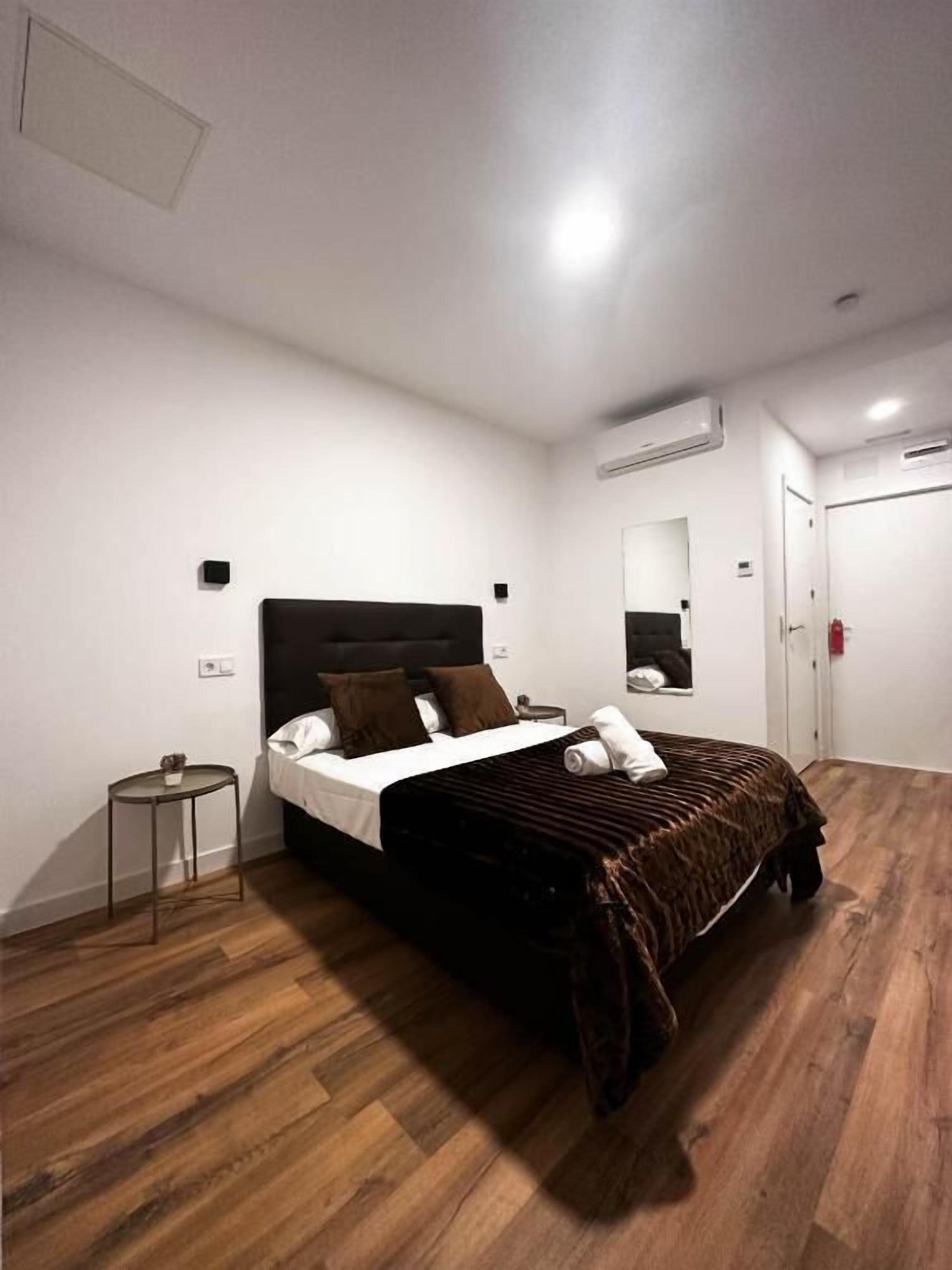 A bedroom with a large bed, a small bedside table, a mirror, and a wardrobe.