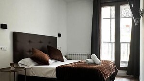 Habitación de hotel moderna con una cama grande, una mesita de noche pequeña y una ventana con cortinas.