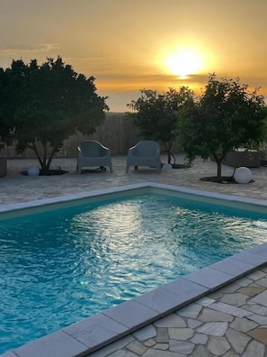 Piscina con dos sillas y árboles, rodeada de baldosas de piedra.