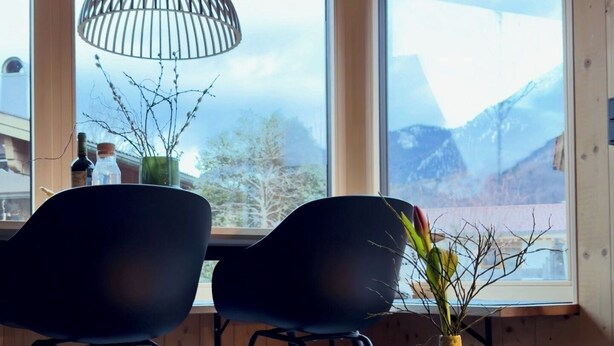 Ein modernes Zimmer mit zwei schwarzen Stühlen, einem runden Tisch, einer Vase mit Zweigen und einer Pendelleuchte.