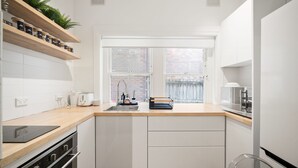 A modern kitchen with white cabinets, a wooden countertop, a window with a view of a brick wall, and a built-in shelf with jars. - Bondi Beachside Escape - Surf & Vibe (Bondi Beach)