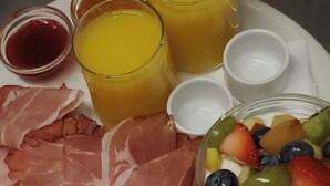 A breakfast plate with ham, cheese, fruit, and juice.