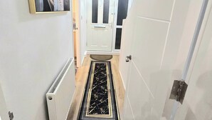 Un couloir avec un radiateur, un tapis aux motifs noirs et dorés et un tableau encadré accroché au mur.