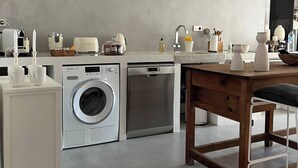 Uma cozinha compacta com máquina de lavar, lava-louças e uma mesa de madeira com uma cadeira.
