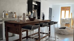 Uma cozinha moderna com ilha central, banquetas, luminárias pendentes e vista para a sala de estar.