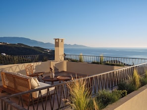 A terrace with outdoor furniture, a view of the sea, and distant mountains. - Eliterra Villa I, Timeless Serenity & Heated Pool (VPW4+V62 Elation, Greece)