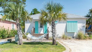 A small, single-story house with a turquoise door and shutters, a hammock in front, and a paved driveway. - 7001 Rookery 3 pools pet friendly Gulf Shores (Gulf Shores)