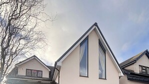 Een modern huis met twee verdiepingen, een garage, grote ramen en een oprit vol met herfstbladeren.