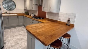 Een moderne keuken met grijze kastjes, een houten aanrechtblad en een ronde spiegel.