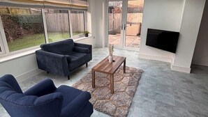 Een ruime woonkamer met een hoge plafond en dakraam, een comfortabele bank, een salontafel en een flatscreen-tv.