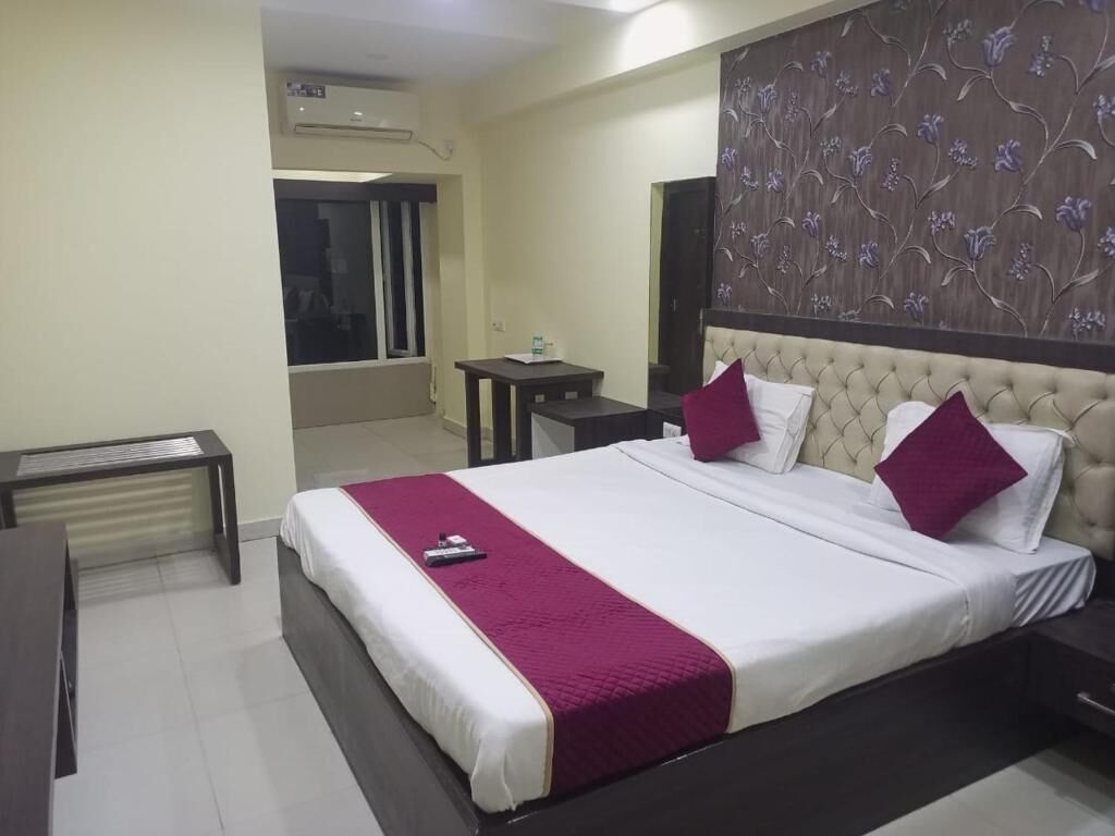 A hotel room with a bed, bedside tables, a desk, and a window.