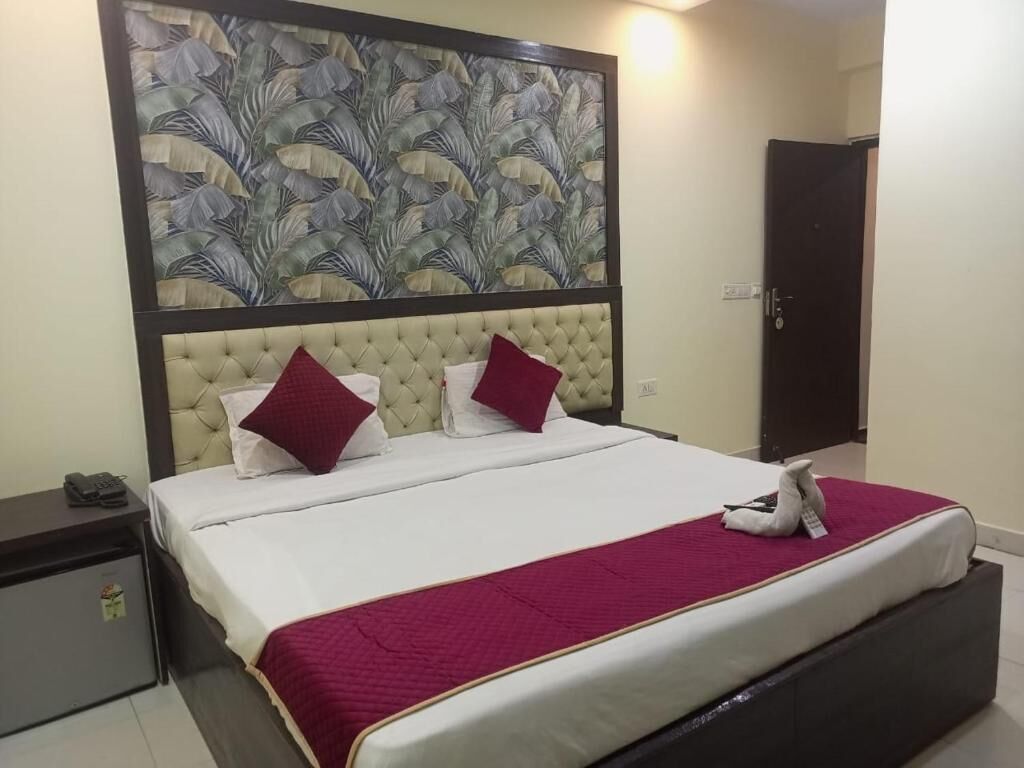 A neatly arranged bedroom with a tufted headboard, two pillows, a red blanket, and a bedside table with a phone.