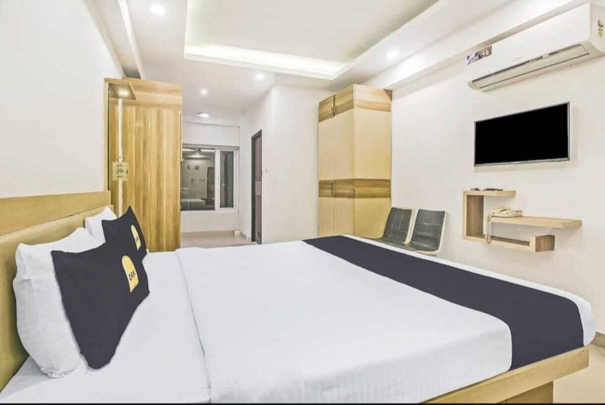 Ένα δωμάτιο ξενοδοχείου με ένα κρεβάτι, μια τηλεόραση τοποθετημένη στον τοίχο, μια ξύλινη ντουλάπα και ένα μικρό ράφι με ένα τηλέφωνο.