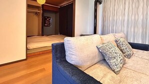 Ein modernes Schlafzimmer mit Schlafsofa, gemusterten Kissen, einer Hängelampe und Blick ins Bad.