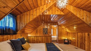 A cozy attic bedroom with wooden walls, a large bed, a fireplace, and a view of the outside. - Mountain Retreat -Hot Tub -Fire Pit -Stevens Pass -River Access -Pet Friendly (Index)