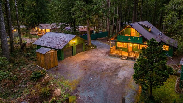 A cabin complex surrounded by dense forest, featuring multiple wooden cabins with attached garages, a central larger cabin with a porch, and a gravel driveway. - Mountain Retreat -Hot Tub -Fire Pit -Stevens Pass -River Access -Pet Friendly (Index)