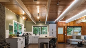 A modern kitchen with white cabinets, a central island, and a wood-burning stove. - Mountain Retreat -Hot Tub -Fire Pit -Stevens Pass -River Access -Pet Friendly (Index)