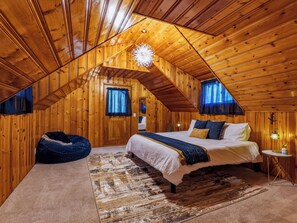 A cozy attic bedroom with a sloped wooden ceiling, a large bed with a white comforter, a blue throw blanket, and a rustic rug. - Mountain Retreat -Hot Tub -Fire Pit -Stevens Pass -River Access -Pet Friendly (Index)