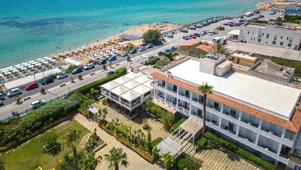 An aerial view of a coastal area with a beach, parking lot, and buildings. - HOTEL JONIO (Noto)