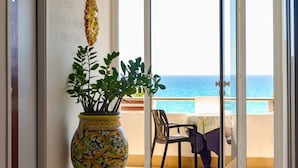 A room with a large decorative vase, a chair, and a table with a view of the sea. - HOTEL JONIO (Noto)