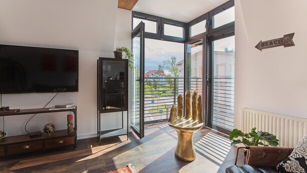Un salón moderno con una televisión grande, suelo de madera, un ventanal que da a un balcón y un cartel con la palabra 'BEACH'.