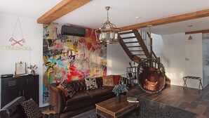 Una sala de estar moderna con un sofá de cuero marrón, una mesa de centro de madera y un mural abstracto colorido en la pared.