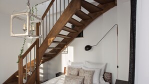 Une chambre avec un escalier en bois, une lanterne suspendue, un lit avec une literie blanche et une table de chevet.