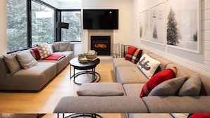 A modern living room with a fireplace, large windows, and a flat-screen TV. - Le Repère du Sommet - Spa (Orford)