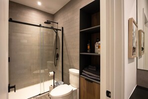 Une salle de bain moderne avec une douche à parois de verre, des toilettes et un meuble-lavabo en bois doté d’étagères.