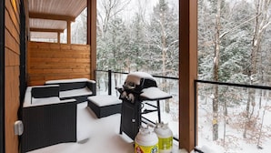A covered outdoor seating area with a grill and propane tanks, overlooking a snowy forest. - Le Repère du Sommet - Spa (Orford)