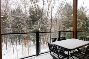 Un balcon enneigé, avec une table et des chaises, donnant sur une forêt.