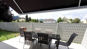 Een terras buiten met een tafel, stoelen, een barbecue en een uitzicht op huizen en bergen.