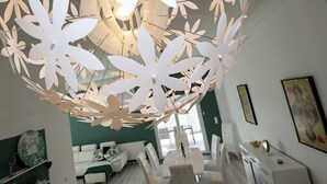 Een moderne woonkamer met een witte bank, een eettafel met stoelen en een decoratieve plafondlamp.