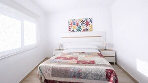 Ein Schlafzimmer mit einem Bett, einem Nachttisch, einer Wandlampe und einem Fenster mit Blick auf Bäume.