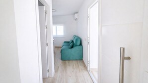 Ein Flur, der zu einem Raum mit einem türkisfarbenen Sofa und einem Fenster führt.