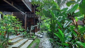 Un escalier en bois mène à un bâtiment traditionnel, lui-même entouré d’une végétation luxuriante.