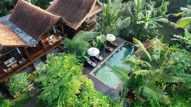 Une villa en bois dotée d’une piscine, le tout entouré d’une végétation tropicale luxuriante.