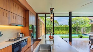 Una cocina moderna con armarios de madera, electrodomésticos de acero inoxidable y un amplio ventanal con vistas a un jardín y piscina.
