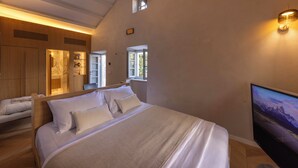 Una habitación de hotel moderna con una cama grande, una zona de estar con sofá, televisión y ventana que proporciona luz natural.