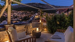 Una terraza con mesas al aire libre, una mesa de piedra y vistas a un pueblo en la ladera al atardecer.