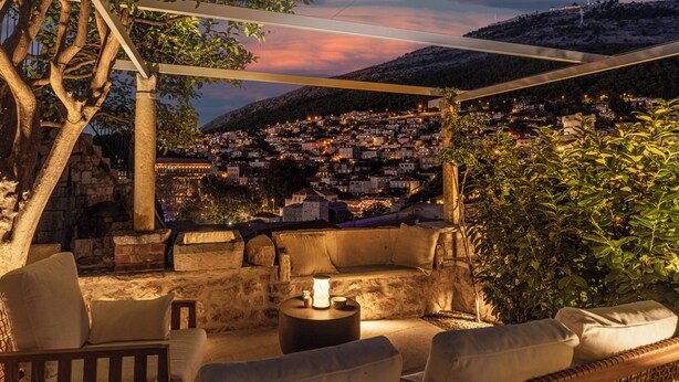 Un área de estar al aire libre con paredes de piedra, vista a un pueblo y una pérgola.